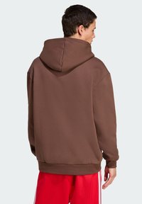 Felpa con cappuccio marrone realizzata in tessuto morbido, con una vestibilità rilassata, polsini e orlo a costine. Presenta un ampio design del cappuccio sul retro senza grafiche.