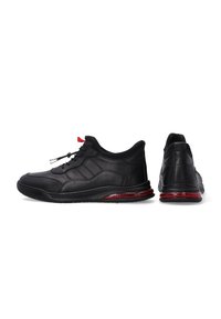 Schwarze Sportschuhe mit einem glatten Obermaterial aus Leder, strukturierten Akzenten, roten Details an der Sohle und einem gepolsterten Kragen für zusätzlichen Komfort.