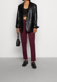 Czarna skórzana marynarka na czarnym koronkowym topie, w zestawieniu z bordowymi spodniami o dopasowanym kroju i czarnymi loafersami. Akcesoria obejmują małą torebkę.