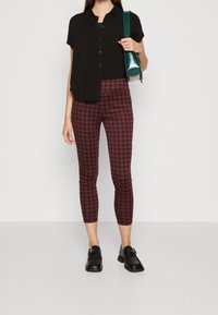 Czarna koszulka z krótkim rękawem, czerwono-czarne legginsy w kratkę sięgające do kostek oraz czarne buty. Ubranie ma dopasowany krój i casualowy styl.