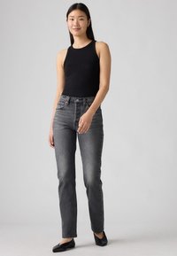 Zwart geribbeld tanktop gecombineerd met hooggeknipte, vervaagde grijze rechttoe-rechtaan jeans en zwarte flats, met een eenvoudig ontwerp zonder patronen.