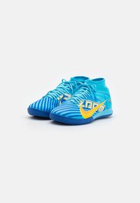 Blå sportskor med hög krage, med ett randigt mönster, gul Nike-logga och strukturerad gummisula.