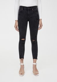 Jeans skinny de mezclilla negra con roturas desgastadas en las rodillas y dobladillos deshilachados, con un corte alto y una textura suave.