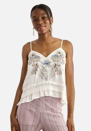 Mujer con camiseta blanca sin mangas con bordado floral y bajo con volantes, combinada con pantalones texturizados de color púrpura claro.