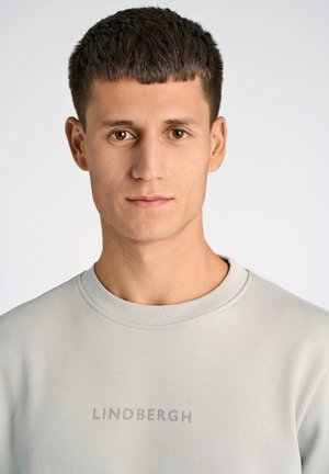 Lysegrå crewneck sweatshirt med en subtil tekstur, med "LINDBERGH" trykt i en kontrasterende farve tværs over brystet.