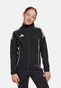 Zwarte sportjack met witte accenten, volledige rits, hoge kraag en het Adidas-logo. Gemaakt van glad, rekbaar materiaal. Voorzien van Aeroready-technologie.