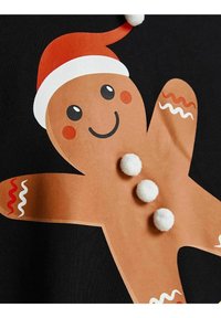 Usmívající se perníkový muž s červenou čepicí Santy, bílými pom-pom knoflíky a dekorativním vlnitým polevou na rukou a nohách na černém pozadí.