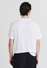 Weißes Mesh-T-Shirt mit Rundhalsausschnitt, überschnittenen Schultern und lockerer Passform. Verfügt über ein strukturiertes Muster und einen abgerundeten Saum.