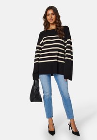 Maglione oversize a righe nero e crema, con scollo quadrato e maniche lunghe, abbinato a jeans azzurri e décolleté nere con cinturino.
