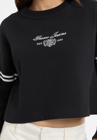 Felpa cropped nera in cotone, con logo ricamato bianco e testo "EST. 1981", dotata di dettagli a strisce sulle maniche.