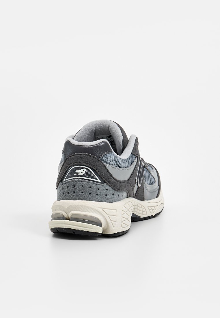 Zapatilla deportiva gris con un upper de malla y ante, cuello acolchado y suela de goma texturizada. Presenta un logo en la parte trasera y lateral.
