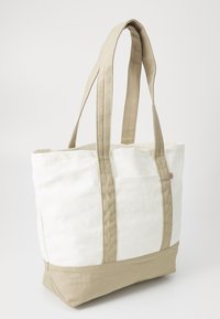 Lerrets tote bag med hvit kropp og beige bunn. Har to robuste håndtak og en liten ekstern lomme. Teksturert stoff for holdbarhet.