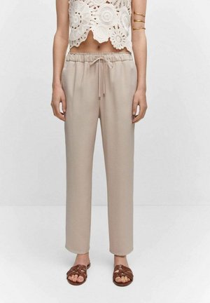 Beige, loose-fitting pants with a drawstring waist, straight legs, and smooth texture. Worn with a white crochet top and brown sandals.