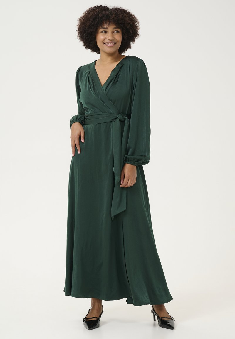 Abito lungo stile avvolgente in satin verde scuro con maniche lunghe e una cintura da annodare in vita. Tessuto liscio; presenta un profondo scollo a V.