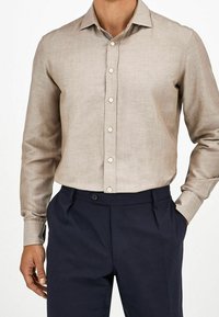 Camicia in lino beige con colletto, davanti con bottoni e maniche lunghe; abbinata a pantaloni blu scuro con tasche laterali e chiusura con bottone.