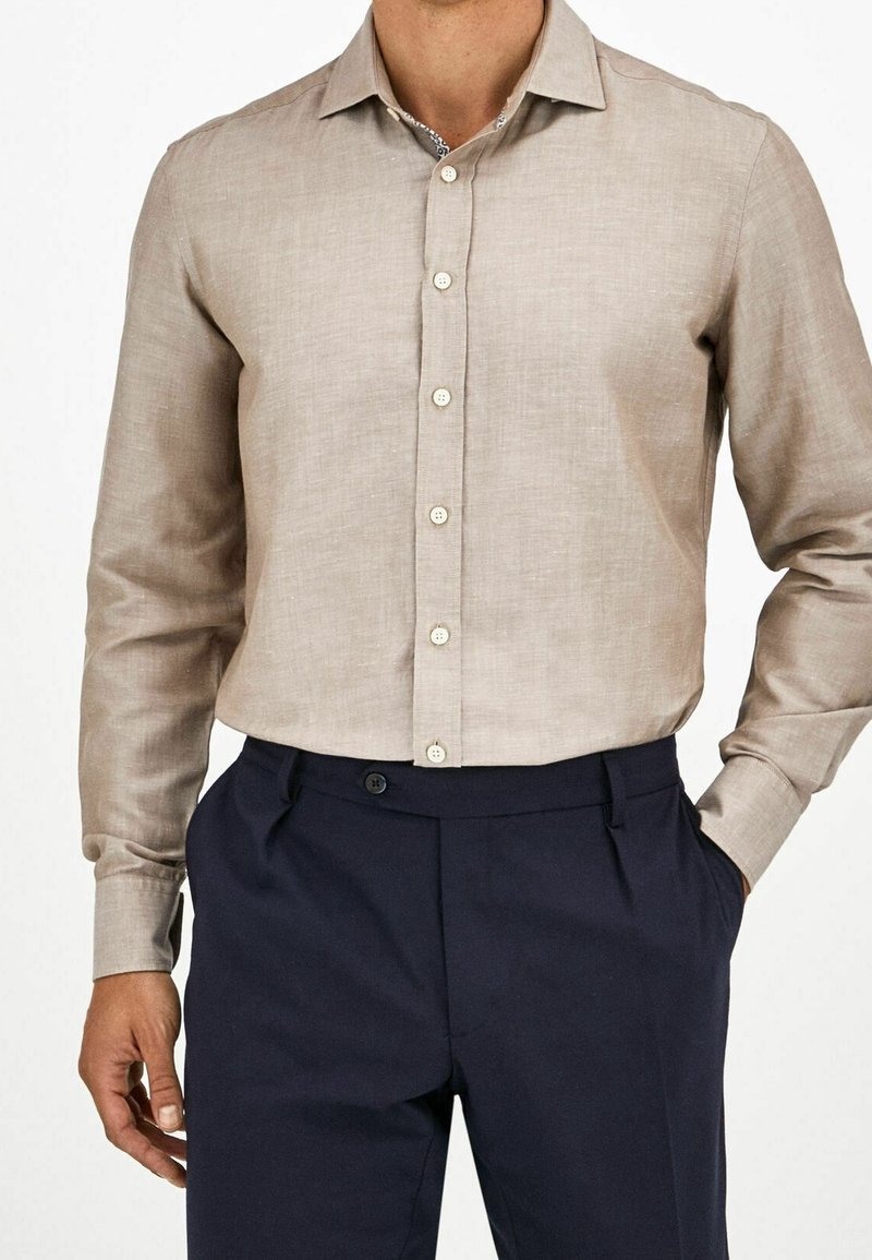 Camicia in lino beige con colletto, davanti con bottoni e maniche lunghe; abbinata a pantaloni blu scuro con tasche laterali e chiusura con bottone.