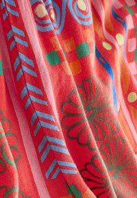 Multifarbener Stoff mit rotem Grund, der florale und geometrische Muster in Grün, Blau, Orange und Pink aufweist, mit einer weichen, strukturierten Oberfläche.