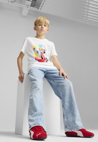 Valkoinen graafinen t-paita, jossa onBold multivärisiä abstrakteja kuvioita, yhdistettynä vaaleansinihin farkkuihin ja punamustiin urheilukenkiin.