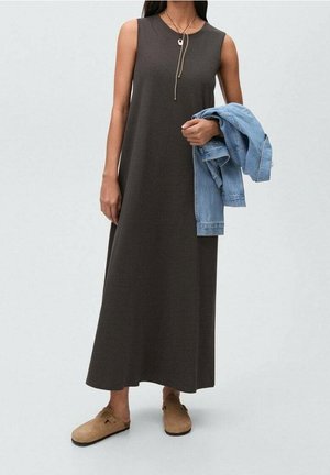 Robe maxi sans manches, de couleur marron foncé, avec une coupe décontractée, un col rond et des fentes latérales discrètes, associée à une veste en denim bleu clair et des chaussures beiges.