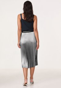Top negro sin mangas combinado con una falda de tubo plateada de longitud a la rodilla. La falda tiene un acabado brillante y sutiles rayas verticales; sandalias de tiras simples.