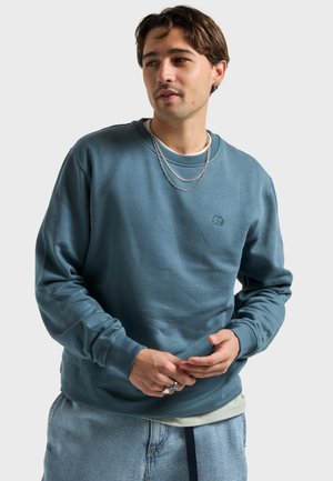 Blauer Rundhalspullover aus weichem Material, mit einem kleinen, erhabenen Elefantenlogo auf der Brust, langen Ärmeln und gerippten Bündchen.