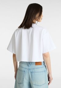 Hvid cropped t-shirt med korte ærmer og en klassisk rund halsudskæring. Sammen med lys blå højtsiddende denimshorts med et lædermærke.