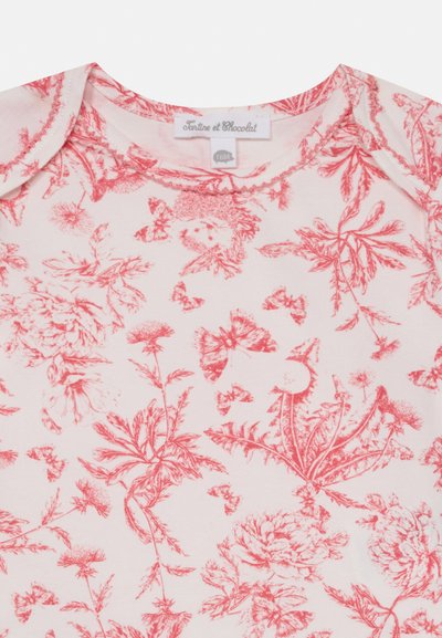 Short-sleeve, pink cotton top with floral and butterfly red print. Features a round neck and delicate stitching on the neckline.