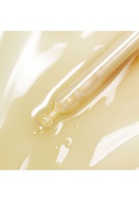 Gros plan d'un compte-gouttes transparent libérant un sérum jaune clair sur une surface lisse et brillante avec de petites gouttes de liquide.