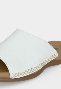 Λευκό δερμάτινο σανδάλι slip-on με μπεζ σόλα και διακοσμητική μπεζ σταυροβελονιά κατά μήκος του άνω άκρου.