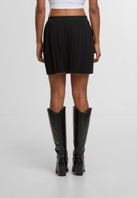 Černá plisovaná mini sukně s elastickým pasem, doplněná černými koženými vysokými botami ke kolenům s špičatou špičkou a blokovými podpatky.