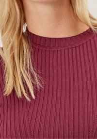 Top a costine bordeaux con scollo rotondo, caratterizzato da righe verticali e dettagli testurizzati. Tessuto morbido e design aderente.