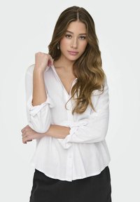Camicia bianca con bottoni realizzata in tessuto leggero, con maniche arrotolate e una vestibilità comoda, abbinata a una gonna nera testurizzata.
