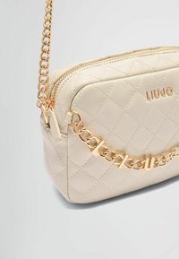Béžová prošívaná kožená crossbody taška s zlatým řetízkem a logem "LIU JO" na přední straně. Zapínání na zip nahoře.