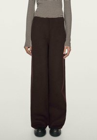 Spodnie o szerokich nogawkach w ciemnym bordowym kolorze, wykonane z miękkiej tkaniny, z wysokim stanem i gładką fakturą. Połączone z czarnymi butami na platformie.