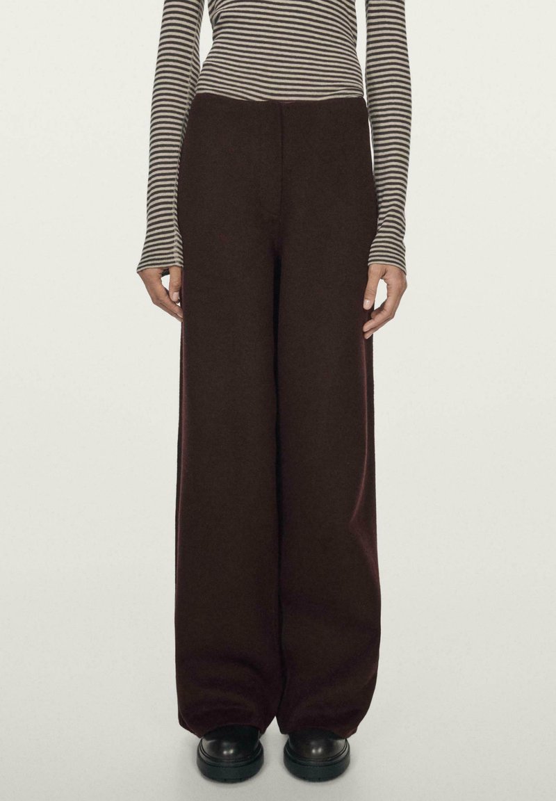 Spodnie o szerokich nogawkach w ciemnym bordowym kolorze, wykonane z miękkiej tkaniny, z wysokim stanem i gładką fakturą. Połączone z czarnymi butami na platformie.