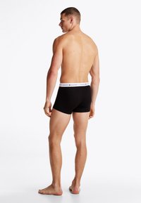 Sorte bomulls boxershorts med hvit midjebånd som har merkevarenavnet. Korte ben og en jevn tekstur. Modell vist fra baksiden.