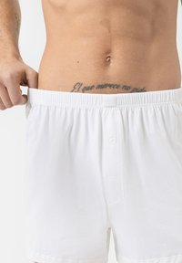 Boxers en coton blanc avec une taille élastique et une braguette à boutons, présentant une texture lisse et une étiquette logo à l'arrière.