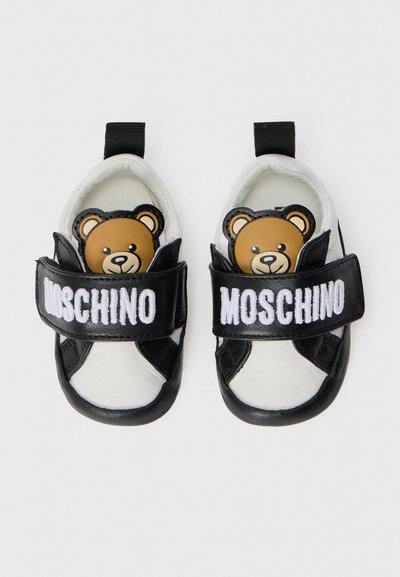Svartvita barnskor med björnmönster, utrustade med kardborreband och tydlig "MOSCHINO"-logotyp på remmen.