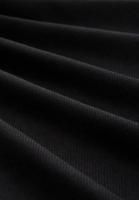 Tessuto nero con una texture a coste, caratterizzato da pieghe diagonali che creano ombre e profondità sottili.
