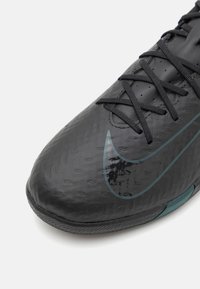 Fekete sportcipő, texturált felülettel, fekete fűzőkkel és egy teal Nike logóval az oldalán, lekerekített orral és gumitalppal.