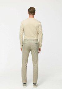 Krémszínű, hosszú ujjú ing, sima textúrával, világosszürke mintás nadrággal párosítva, amely testreszabott szabással és hátsó zsebekkel rendelkezik. Fehér sportcipők.