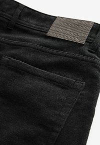 Zwarte stoffen broeken met een gestructureerde afwerking, voorzien van een geweven patroonlabel op de tailleband en een achterzakdetail.