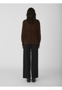 Brun kabelstrik sweater med en afslappet pasform, parret med brede sorte bukser og sorte platform sko. Enkel, struktureret design på sweateren.