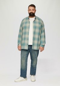 Koszula w kratę zapinana na guziki w jasnoturkusowym i kremowym kolorze, noszona na białym t-shircie. Niebieskie dżinsy i białe trampki dopełniają strój.