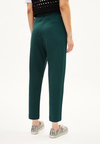 Groene joggingsbroek met elastische tailleband, gevormde benen en een achterzak; gecombineerd met gestreepte sneakers. Glad textuur van de stof.
