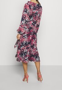 Blommig midiklänning i marinblått, med rosa och vita blommor, långa puffärmar, en knytning i midjan och en utsvängd fåll. Bärs med rosa klackar.