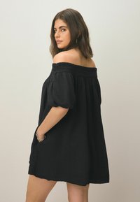 Zwart off-shoulder jurk van textuurstof, met poffende mouwen en zijzakken; relaxte pasvorm met een zoom die boven het midden van de dij valt.