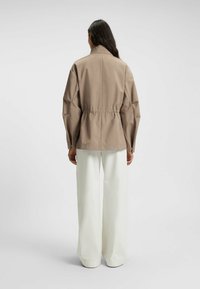 Giacca beige con vita arricciata, maniche lunghe e colletto. Abbinata a pantaloni bianchi a gamba larga. Tessuto liscio, design minimalista.