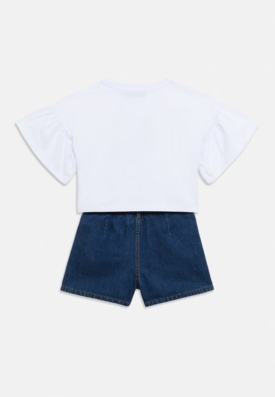 Λευκό κοντομάνικο μπλουζάκι με φουσκωτά μανίκια, σε συνδυασμό με σκούρα μπλε τζιν σορτς με φερμουάρ μπροστά και τελειώματα με ρέλι.