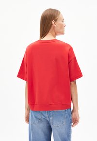 Roter übergroßer Pullover mit kurzen Ärmeln und rundem Halsausschnitt, der eine glatte Textur aufweist. Kombiniert mit hellblauen Jeans.